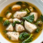 A bowl of chicken and chard soup with tender chicken pieces, vibrant green chard, and a savory broth, served with a slice of crusty bread.